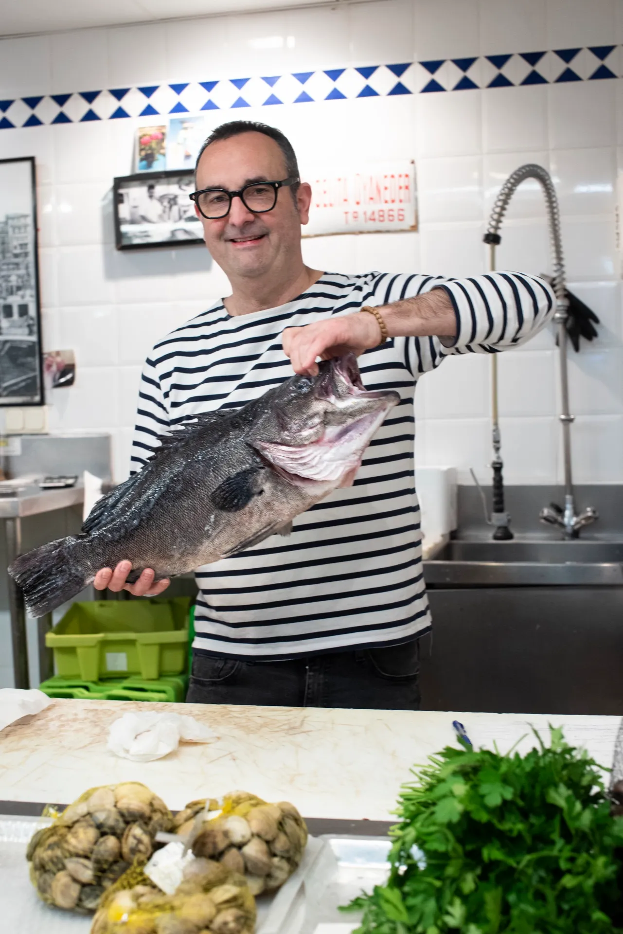 Chef Ben holding a large fresh fish at a market fish stall in San Sebastián